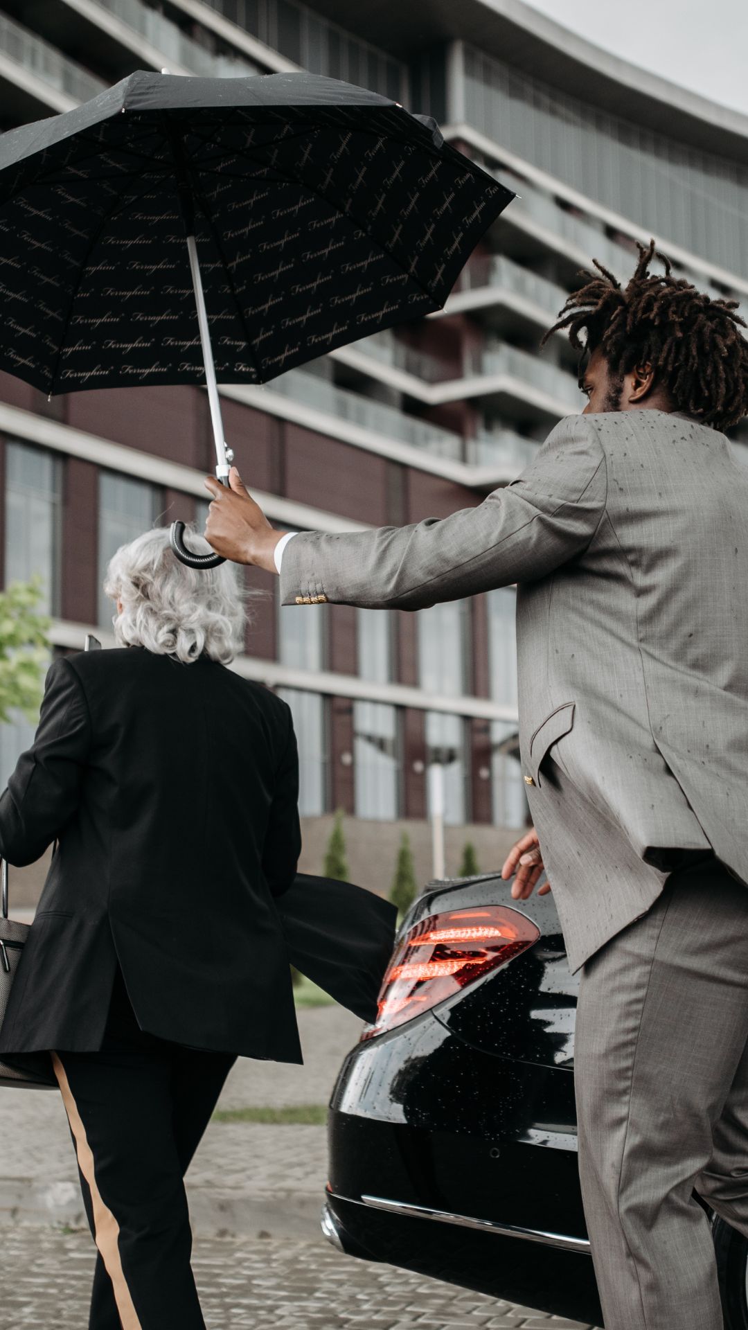 Private Chauffeur Service holding umbrella next to car for client